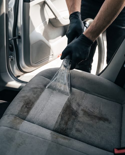 An extraction tool pressed into a soiled cloth car seat with a clean band emerging.