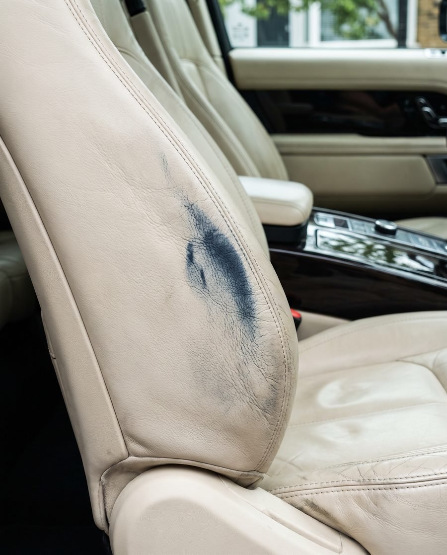 A cream leather car seat with a blue denim dye transfer stain worked into the grain.