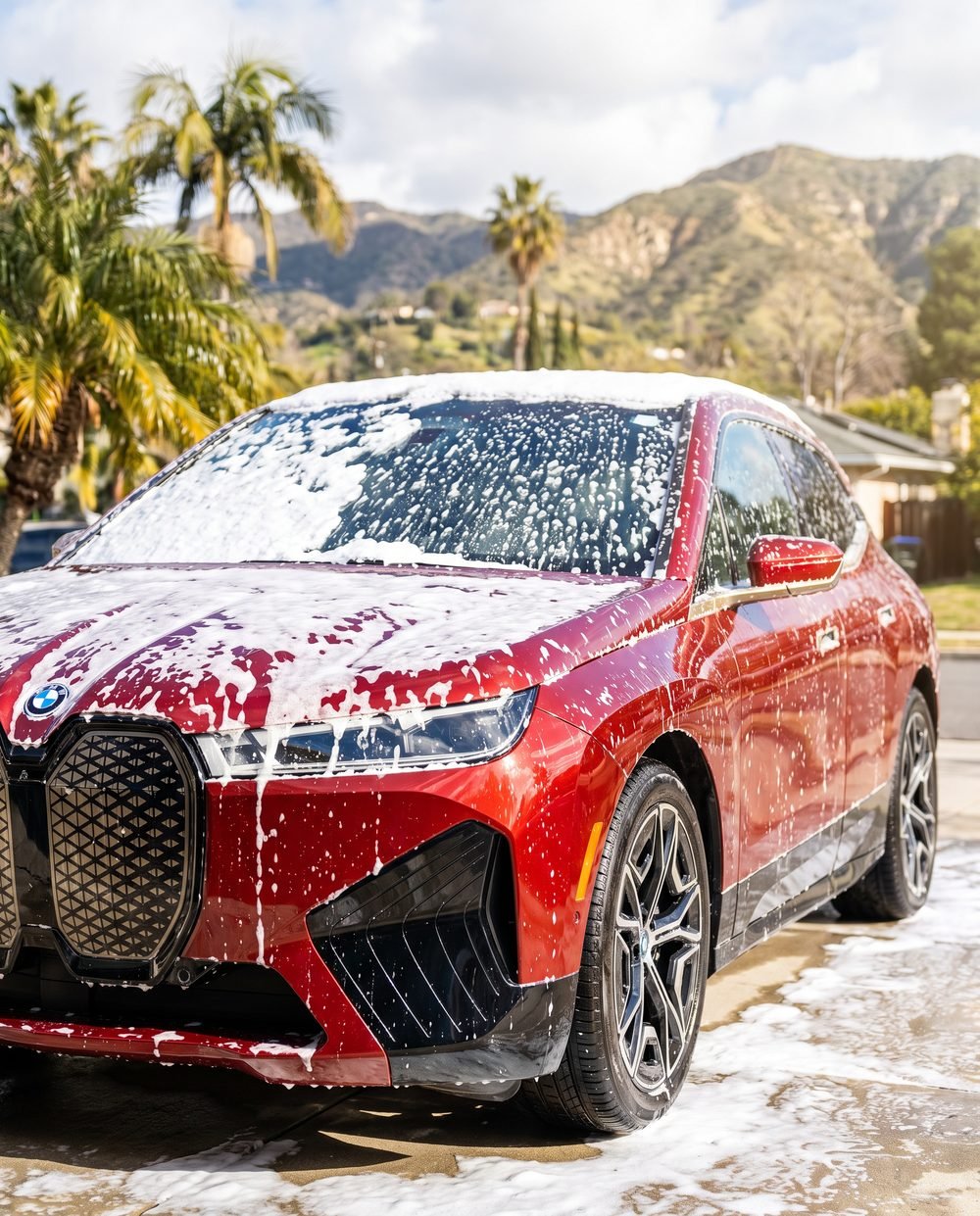 Thick foam covering the hood and roof of a red BMW iX in a Pasadena driveway.
